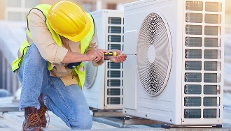 Technicien Réparation Climatisation CVC Unité Extérieure Technicien CVC en casque jaune et gilet fluorescent répare une unité de climatisation extérieure avec un tournevis.